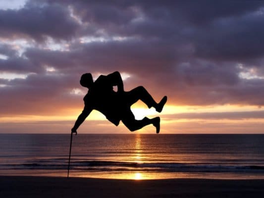 Mann springt seitlich mit Stock und Hut vor Sonnenuntergang – Symbol für WOW-Faktor in Verkauf und Marketing