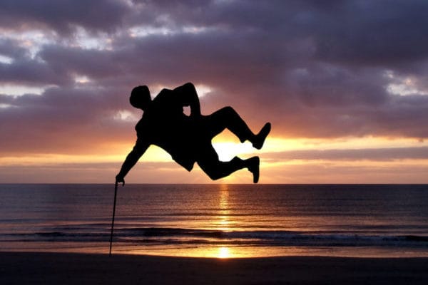 Mann springt seitlich mit Stock und Hut vor Sonnenuntergang – Symbol für WOW-Faktor in Verkauf und Marketing